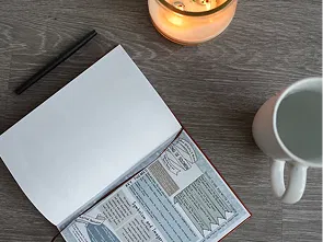 Open Bible study journal on a wooden table next to a candle and a cup